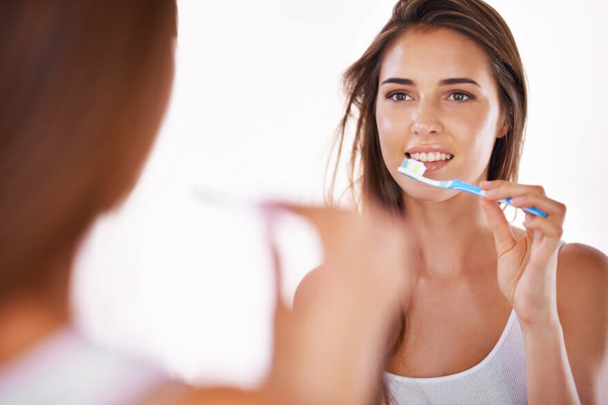 young woman brushing teeth in the mirror