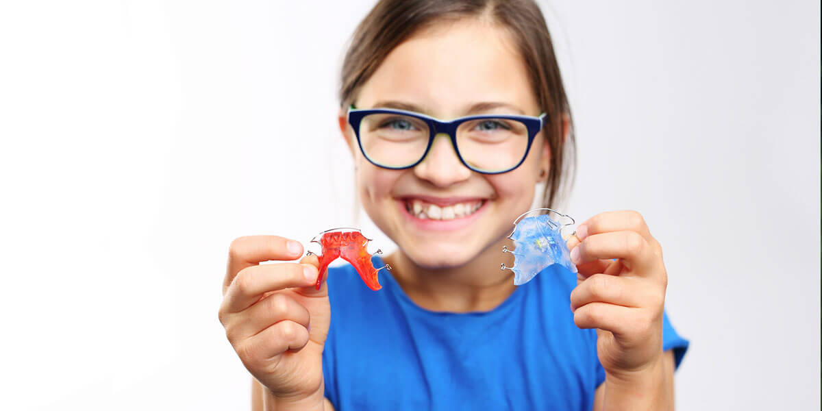 young girl wearing glasses showing two different types of retainers